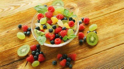 From above glass bowl with assortment of fruits on light wooden table 
