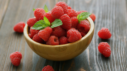 Closeup fresh red raspberry with green leaves in wooden bowl on dark table 