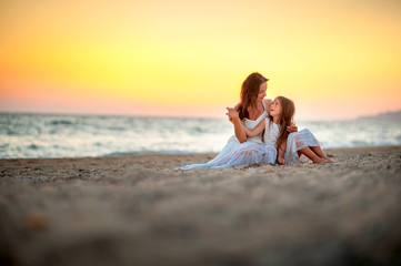 Mom with a little daughter on the beach at sunset, sitting on the sand and resting