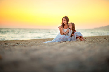 Fototapeta na wymiar Mom with a little daughter on the beach at sunset, sitting on the sand and resting