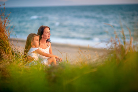 mom and daughter rest on the beach, sit on the beach and watch the sunset