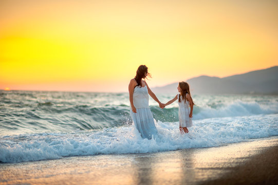 mother walks with her daughter on the beach at sunset, hold hands and walk on the waves
