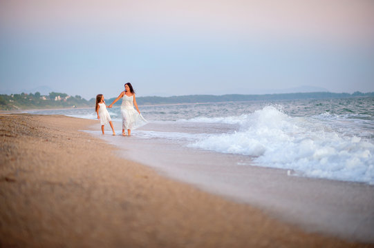 mother walking with her beloved daughter on the beach at sunset, holding hands and smiling