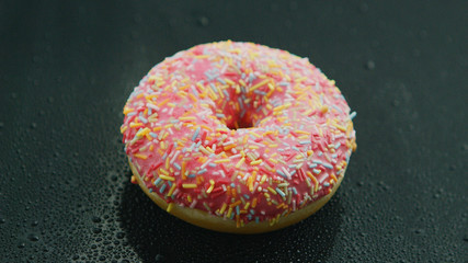 From above appetizing sweet donut with pink glazing and sprinkles on dark background 
