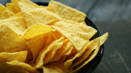 Closeup black plate full of crunchy golden nachos on wooden table 