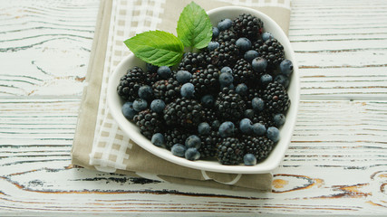 From above blueberry and blackberry with green leaf in heart shaped bowl on wooden background