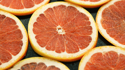 Closeup of composed round slices of cut grapefruit of bright ret color arranged together on glass surface