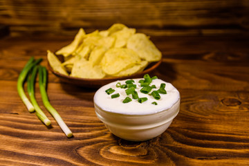 Ceramic plate with potato chips and glass bowl with sour cream on wooden table