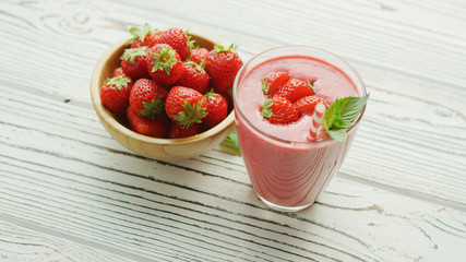 From above shot of glass filled with pink smoothie and served on wooden table with bowl full of red ripe strawberry