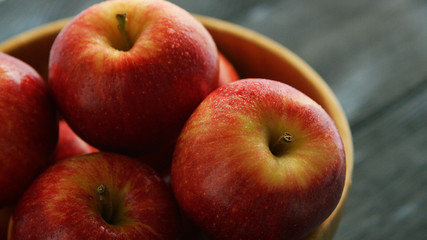Closeup shot of bowl filled with plenty whole red apples with shiny skins in daylight