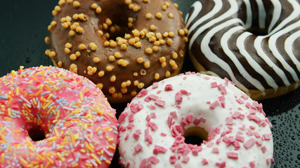 Closeup shot of arranged round doughnuts with different glaze and toppings served on glass surface