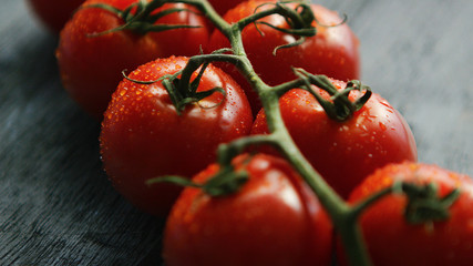Closeup shot of green twig with ripe grapevine tomatoes in drops of water composed on wooden table