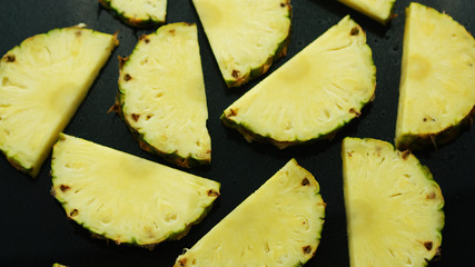 From above closeup shot of half cut unpeeled pineapple pieces on dark background 