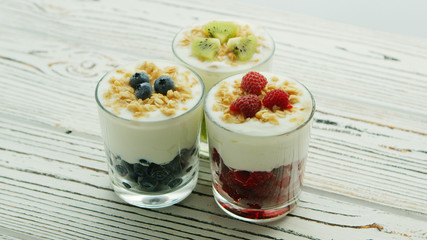 Glass cups with berries in assortment and fresh white yogurt topped with granola and served on wooden table