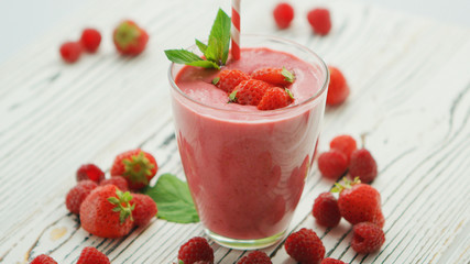 Served glass with fresh strawberry smoothie topped with small berries and mint leaf on wooden table