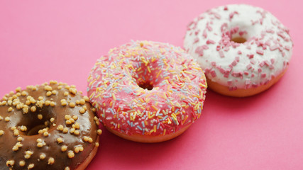 Composed row of delicious assorted doughnuts with different glaze and toppings served on pink background