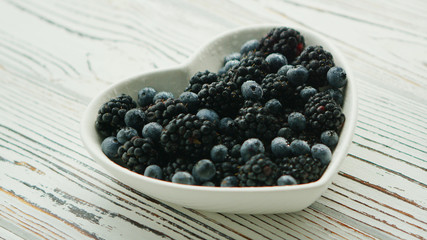 Closeup shot of heart-shaped bowl filled with assortment of blackberries and blueberries on wooden table