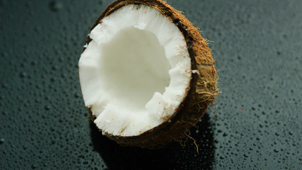 Closeup shot of delicious white coconut half in rough brown shell lying on wet glass surface