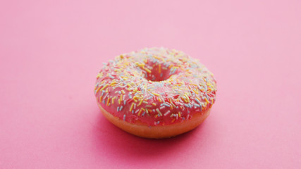 Closeup shot of one delicious sweet doughnut with pink glaze and colorful sprinkles lying on pink background