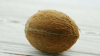 Closeup of textured unpeeled coconut in brown shell lying on white wooden table in soft daylight