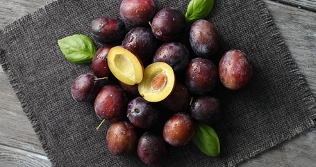 From above view of ripe shiny plums with green basil leaves composed on clean napkin on wooden table