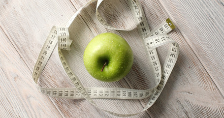 From above shot of composed green fresh apple and measuring tape for weight loss concept on top of wooden table