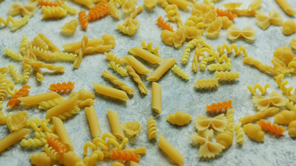 From above view of yellow and orange macaroni of different shape laid in mess on light gray background