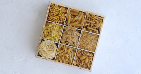 From above view of white box divided into sections with macaroni of different shape on white background