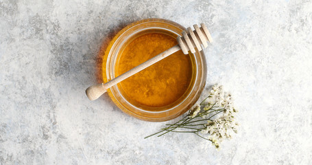 From above view of bowl full of yellow honey with spindle decorated with herb on white background