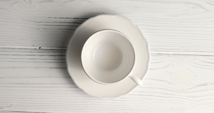 From above view of white empty cup with saucer laid on wooden background