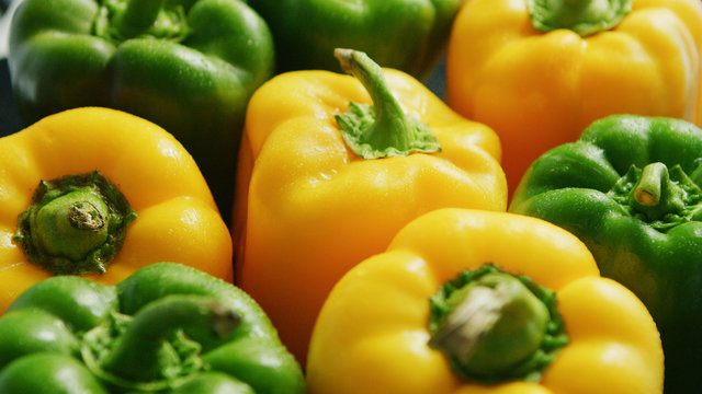 Closeup of composed bunch of shiny wet bell peppers of green and yellow colors in water drops