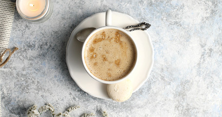 From above shot of coffee with froth in white cup on saucer with silver spoon and white macaron on table