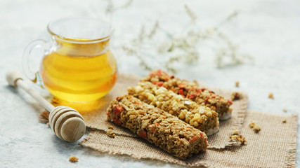 Composed few cereal bars on canvas napkins with glass jar of golden honey near