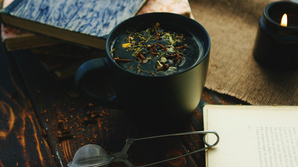 Black mug with fresh tea leaves on water composed on table with books