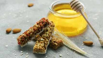 Sweet cereal bars on gray surface in arrangement with jar of honey and wheat ears near