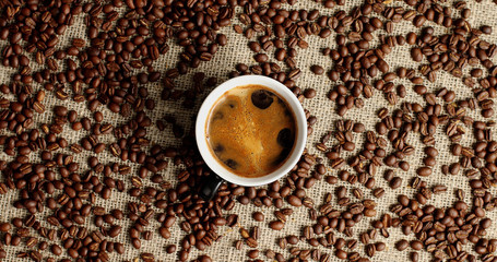 Top view of mug with black coffee on canvas textile covered with roasted coffee beans
