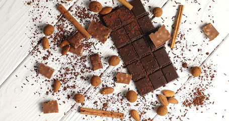 From above view of arrangement with bar of dark chocolate on white wooden table with cocoa and nuts and cinnamon sticks