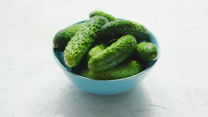 Closeup of small bowl filled with shiny small green cucumbers in soft light on white background