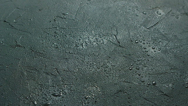 Abstract background of rough gray stone surface covered with water drops shining in daylight