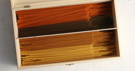 From above of wooden box filled with assorted multicolored spaghetti and lying on white table