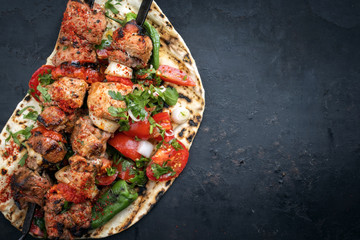 Traditional Greek souvlaki barbecue skewer with tomato, onion and paprika as closeup on a old board...