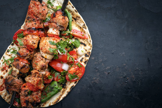 Traditional Greek souvlaki barbecue skewer with tomato, onion and paprika as closeup on a old board with copy space right