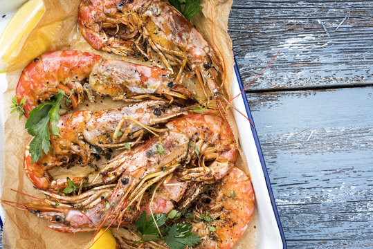 Traditional fried black tiger prawn with lemon and white wine as top view in a white casserole on a wooden blue board with copy space right