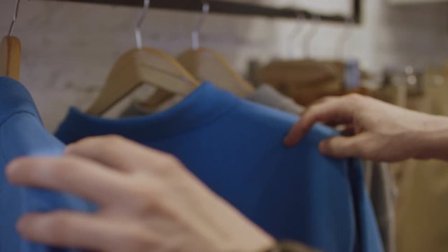 Buyer Chooses pullovers in Clothing Boutique with male Clothes on the hangers.