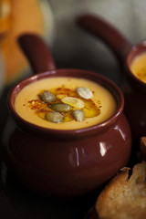 Autumn homemade cream soup of roasted pumpkin with croutons or toasted bread and seeds in a vintage ceramic bowls for Halloween or Thanksgiving day close-up on dark background