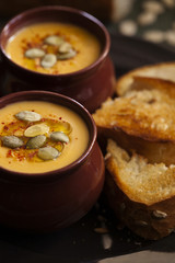 Autumn homemade cream soup of roasted pumpkin with croutons or toasted bread and seeds in a vintage ceramic bowls for Halloween or Thanksgiving day close-up on dark background