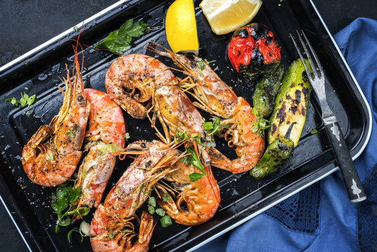 Traditionelle barbecue Black Tiger Garnelen mit Gem&uuml;se und Zitrone als Draufsicht auf einer schwarzen Kasserolle  
