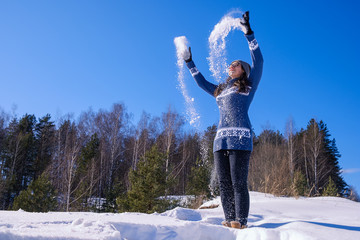 girl in a warm sweater throws snow and bask in the winter sun