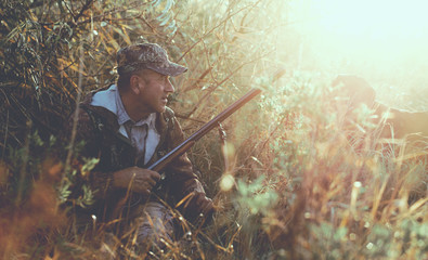 Silhouette of a hunter with a gun in the reeds against the sun, an ambush for ducks with dogs