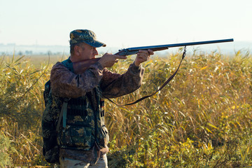 Fototapeta premium Silhouette of a hunter with a gun in the reeds against the sun, an ambush for ducks with dogs